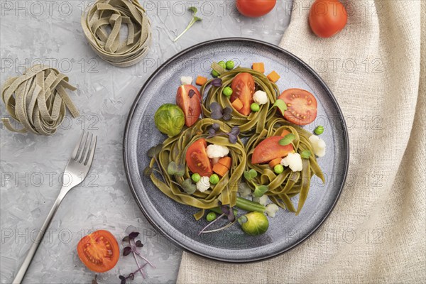 Tagliatelle green spinach pasta with tomato, pea and microgreen sprouts on a gray concrete