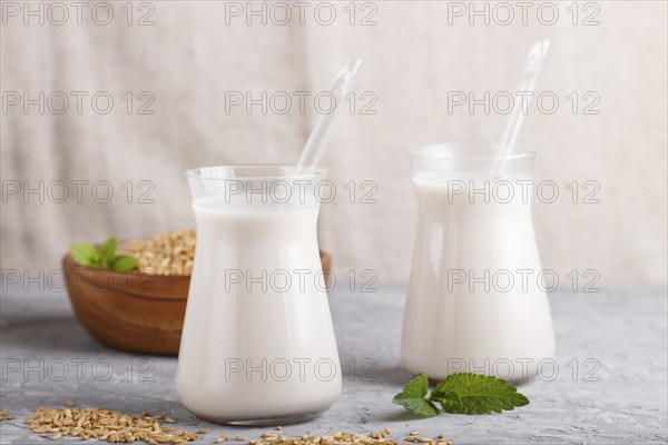 Organic non dairy oats milk in glass and wooden plate with oats seeds on a gray concrete background