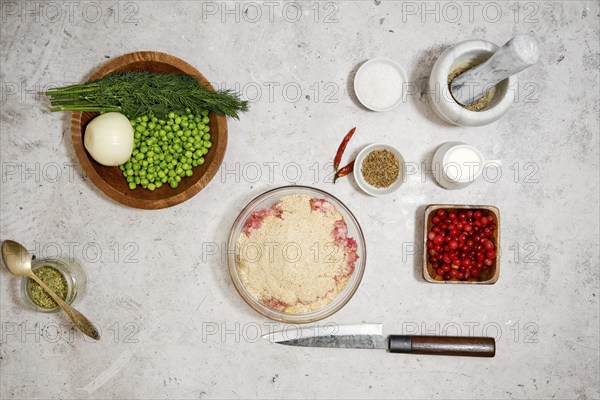Top view of bowl with minced meat, egg and breadcrumbs surrounded with cranberry and green peas for