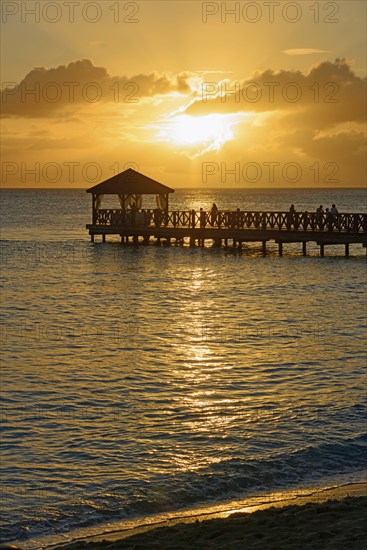 People on a jetty watching the sunset over the sea with beautiful reflection on the water,