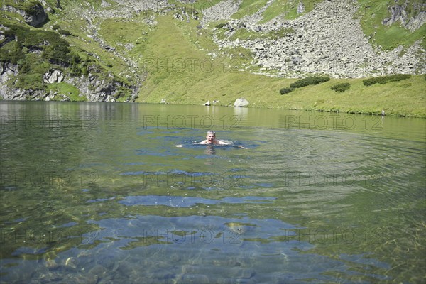 Hiker swimming in the ice-cold mountain lake Mittlerer Kaltenbachsee, Sölktäler Nature Park,