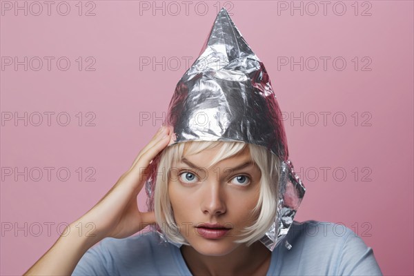 Young woman weraing a tin foil hat on pink studio background. KI generiert, generiert, AI generated