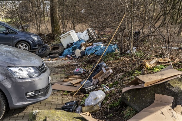 Illegal waste disposal in a car park, in a wooded area, tyres, furniture, refrigerators, household
