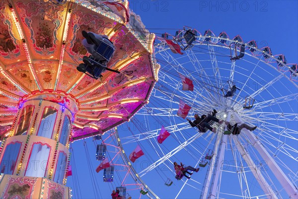 Illuminated chain carousel and Ferris wheel at night with cheerful people, funfair, wave flight,