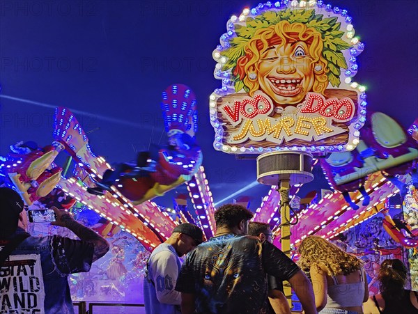 People in front of the illuminated carousel Voodoo Jumper at night, Cranger Kirmes, Herne, Ruhr