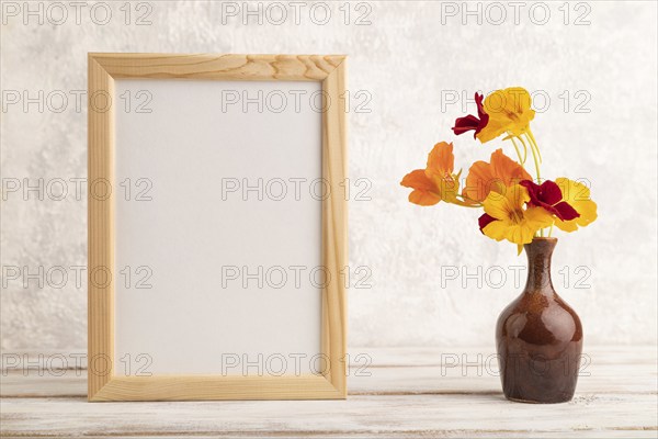 Wooden frame with orange nasturtium flowers in ceramic vase on gray concrete background. side view,