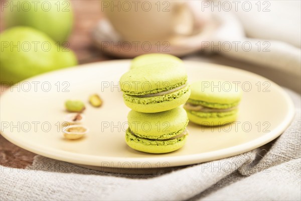 Green macarons or macaroons cakes with cup of coffee on a brown concrete background and linen