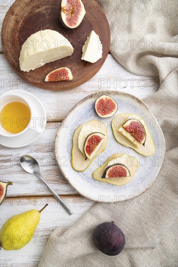 Summer appetizer with pear, cottage cheese, figs and honey on a white wooden background and linen