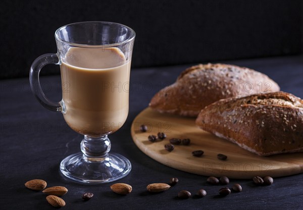 Glass cup of coffee with cream and buns on a black background. close up