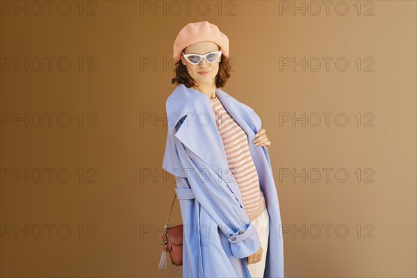 Lovely woman in coral beret and blouse, blue raincoat and sunglasses posing outdoor
