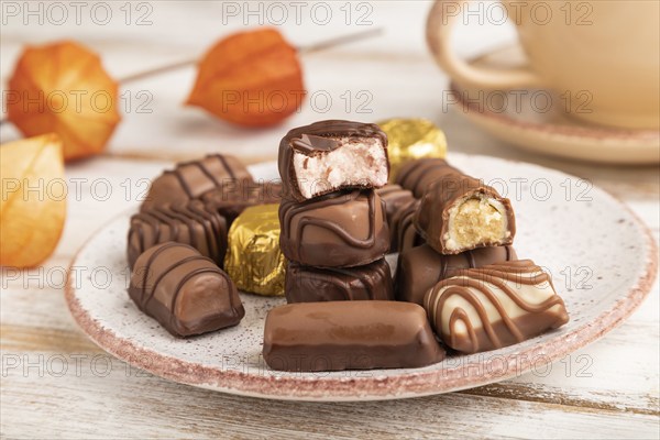 Chocolate candies with cup of coffee and physalis flowers on a white wooden background and orange