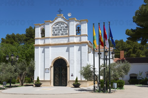 Historische Kapelle mit verschiedenen Fahnen und Bäumen unter blauem Himmel, Ermita y museo Virgen
