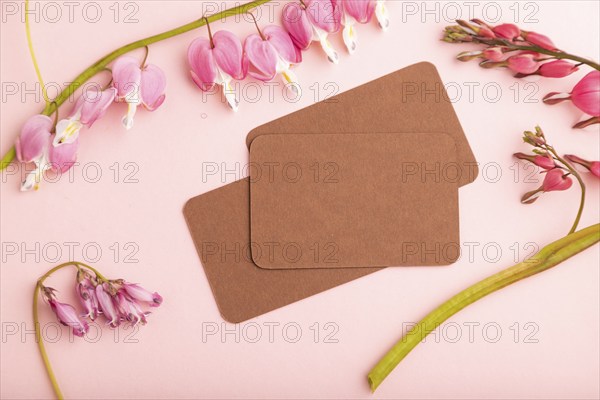 Brown business card with pink dicentra, broken heart flowers on pink pastel background. top view,