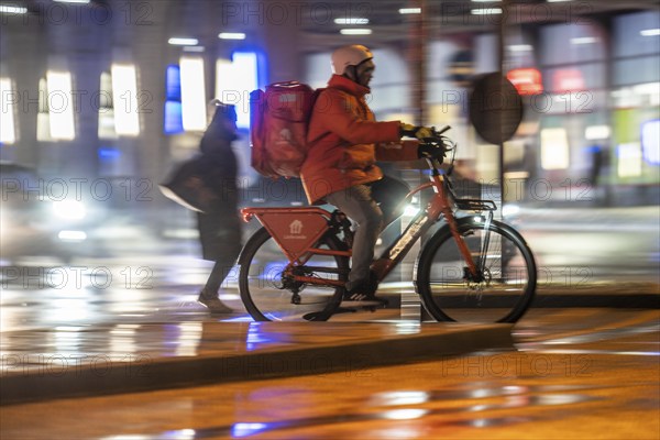 Street at the main station, Lieferando courier, cyclist, rainy weather, city centre, in the