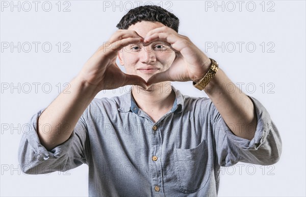 Handsome young man making heart shape with hands isolated. Smiling latin man making heart shape