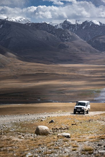 Off-road vehicle on a gravel track, glaciated and snow-covered peaks, Ak Shyrak Mountains, near