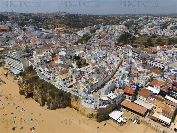 Coastal town with many white buildings on cliffs on the beach, sandy beach with bathers, aerial