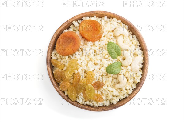 Bulgur porridge with dried apricots, raisins and cashew in wooden bowl isolated on white background