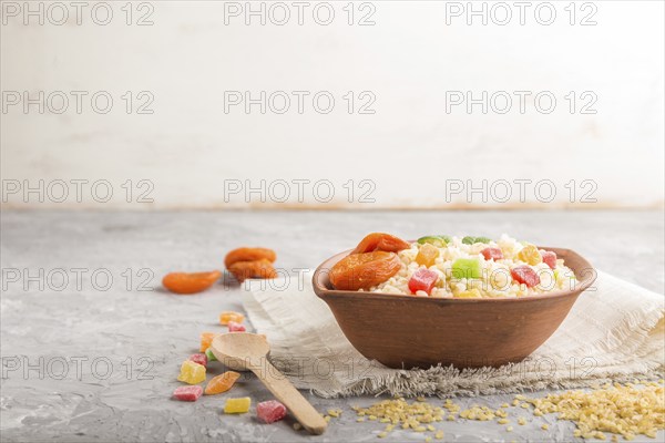 Bulgur porridge with dried apricots and candied fruits in clay bowl on a gray concrete background