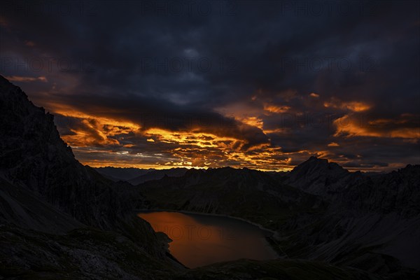 Lake Lüner See with Montafon mountains and dramatic cloudy sky at sunrise, Tschagguns, Rätikon,