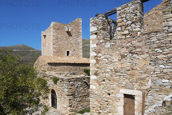 Two stone buildings of a historic village structure under a clear sky, residential towers, Vathia,