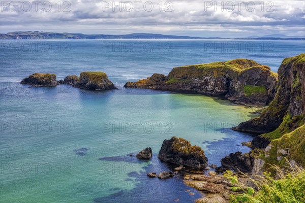 Steep cliffs overlook the clear blue-green sea under dramatic skies, County Antrim Coast