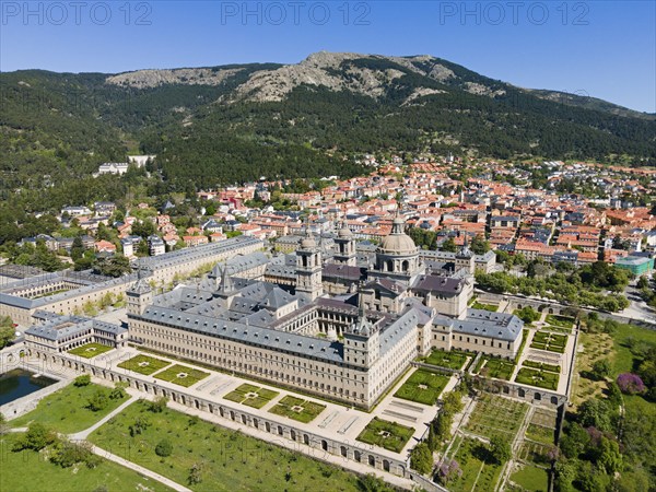 Historic monastery and neighbouring town, surrounded by green landscape and mountains, seen from
