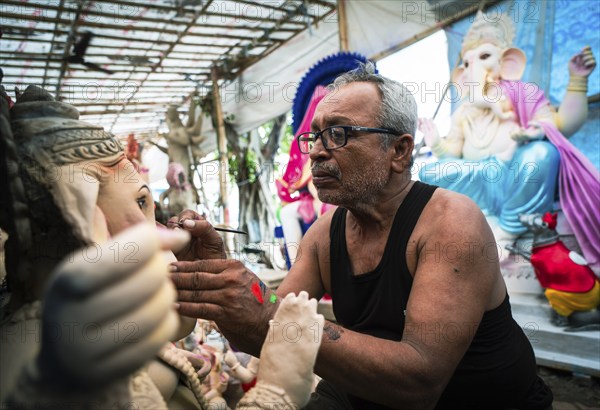 An artisan gives final touches to an idol of the elephant-headed Hindu deity Ganesha at a workshop