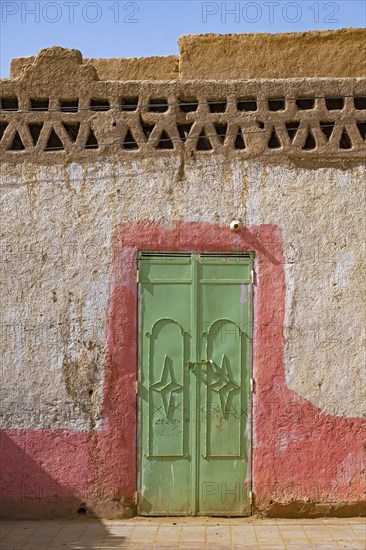 Green iron door in wall of traditional house made of mud and straw in the village Merzouga in the