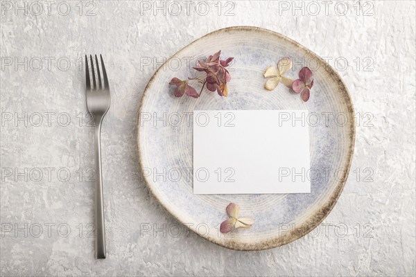 White paper invitation card, mockup with dried hydrangea flowers on ceramic plate and gray concrete