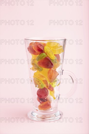 Various fruit jelly candies in drinking glass on pink pastel background. side view, close up