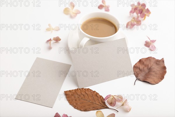 Composition with gray paper business card, brown beech autumn leaves, hydrangea flowers and cup of