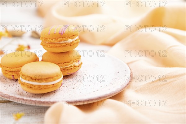 Orange macarons or macaroons cakes with cup of apricot juice on a white wooden background and