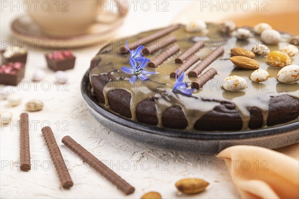 Homemade chocolate brownie cake with caramel cream and almonds with cup of coffee on a white