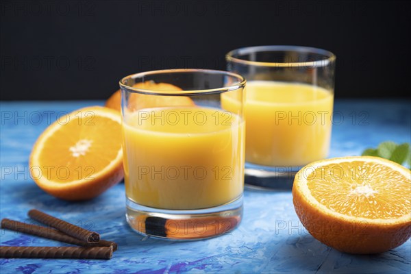 Glass of orange juice on a black and blue background. Hard light, contrast. Side view, close up