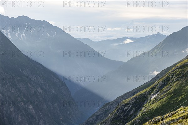 Atmospheric mountain landscape, sunbeams fall between peaks into a mountain valley, evening light,