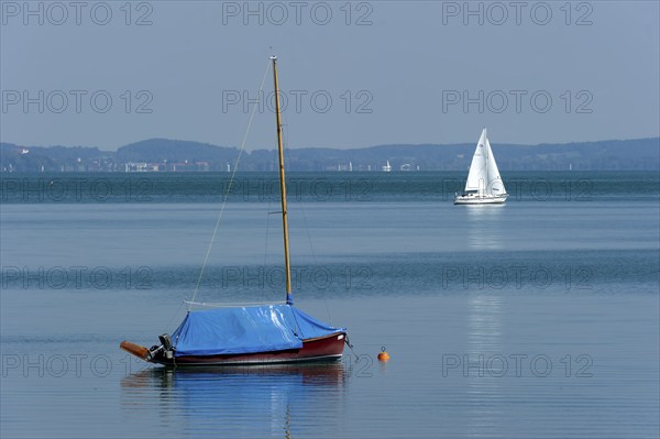 Covered and sailing boat underway on calm waters, Bernried am Starnberger See, Upper Bavaria,
