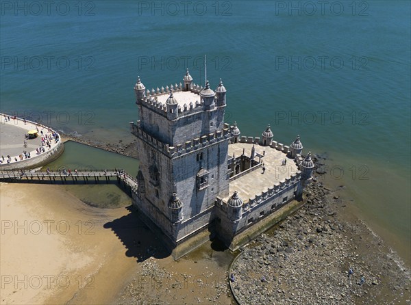 A historic tower by the sea, standing on a rocky sandy beach, with blue sky above, aerial view,