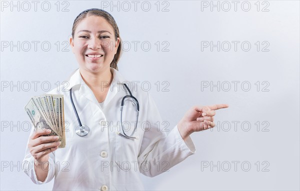 Happy female doctor holding money and pointing to side. Beautiful female doctor showing money and
