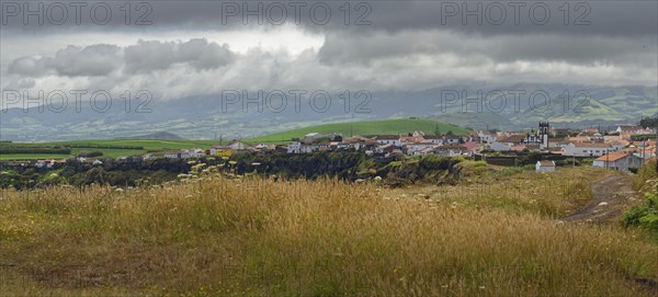 Coastal village on a hill, surrounded by green fields, under a cloudy sky, Fenais da Luz, Sao