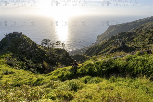 Young man looking out to sea on cliff, evening mood, green coastal landscape on cliff, sea and