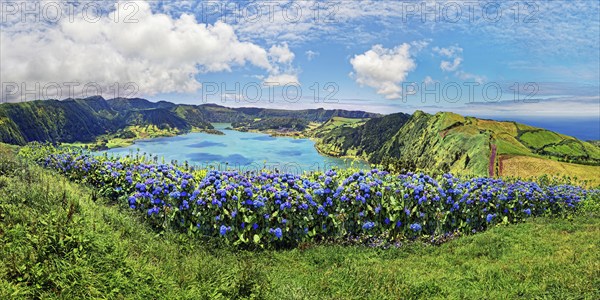 Panoramic view of the crater lake Lagoa Azul with the green overgrown crater rim surrounded by blue