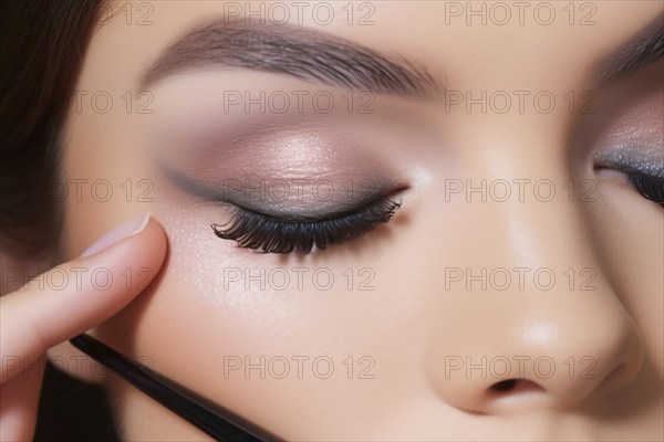 Close up of woman doing eyemakeup with gray and pink eyeshadow and long black fake eyelashes. KI
