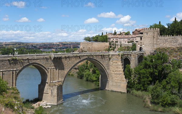 Historic stone bridge over river in rural setting with neighbouring old buildings, Puente de San