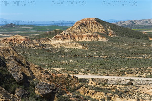 Vast landscape with rocky hills and a road under a clear blue sky, Bardenas Reales Natural Park,