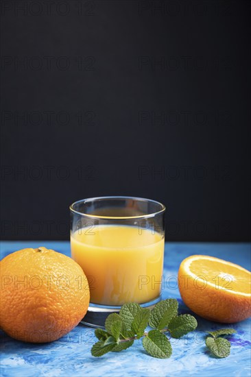 Glass of orange juice with mint on a black and blue background. Hard light, contrast. Side view,