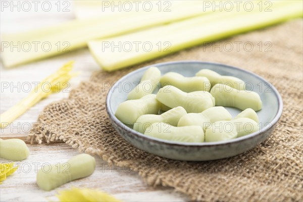 Jelly celery candies on white wooden background and linen textile. close up, side view, selective