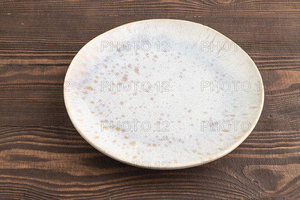 Empty blue and gold ceramic plate on brown wooden background. Side view, copy space