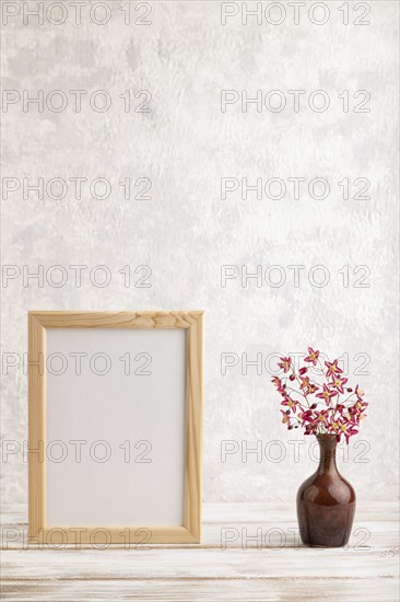 Wooden frame with purple barrenwort flowers in ceramic vase on gray concrete background. side view,