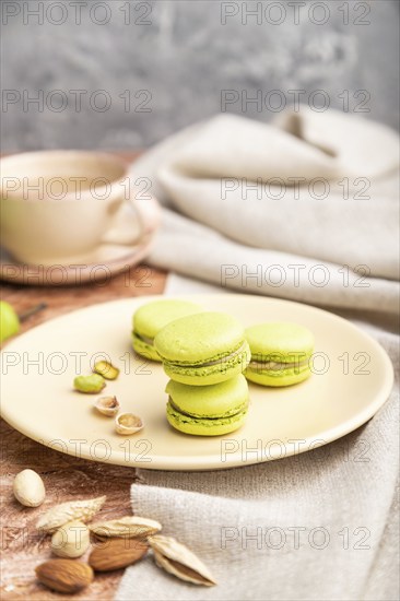 Green macarons or macaroons cakes with cup of coffee on a brown concrete background and linen